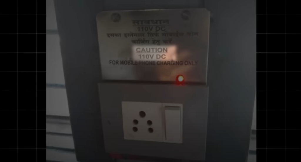 A charging port in an Indian train compartment with a sign discouraging night-time charging. Indian Railways operates on DC (Direct Current) power for lighting and essential functions, which may overheat AC-compatible devices like phones and laptops. Charging electronics at night can lead to battery issues and potential safety risks, so passengers are advised to limit charging to daytime hours when safety is actively monitored.






